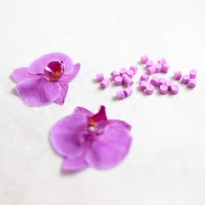 موم‌های گرانول مهروموم در رنگ صورتی در کنار یک گل صورتی